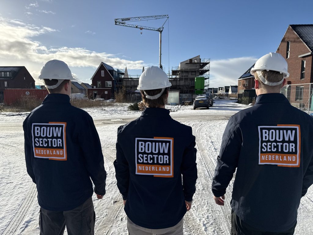 Drie vakmensen van Bouwsector Nederland met witte helm kijken naar nieuwe huizen in aanbouw